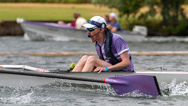 Cox in purple shirt calling out to his crew during a race at Henley